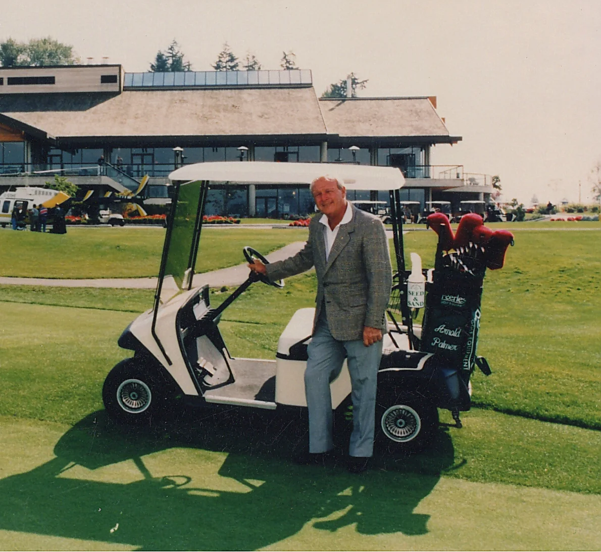Arnold Palmer smiling and standing in front of a golf cart and the Northview clubhouse